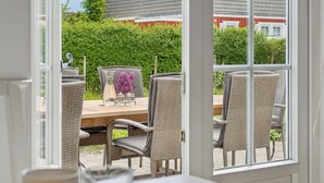 An open door leading to an outdoor dining area with wicker chairs and a table set with glassware and flowers. - Renovated summer house in Vejby/ Tisvilde (Vejby)