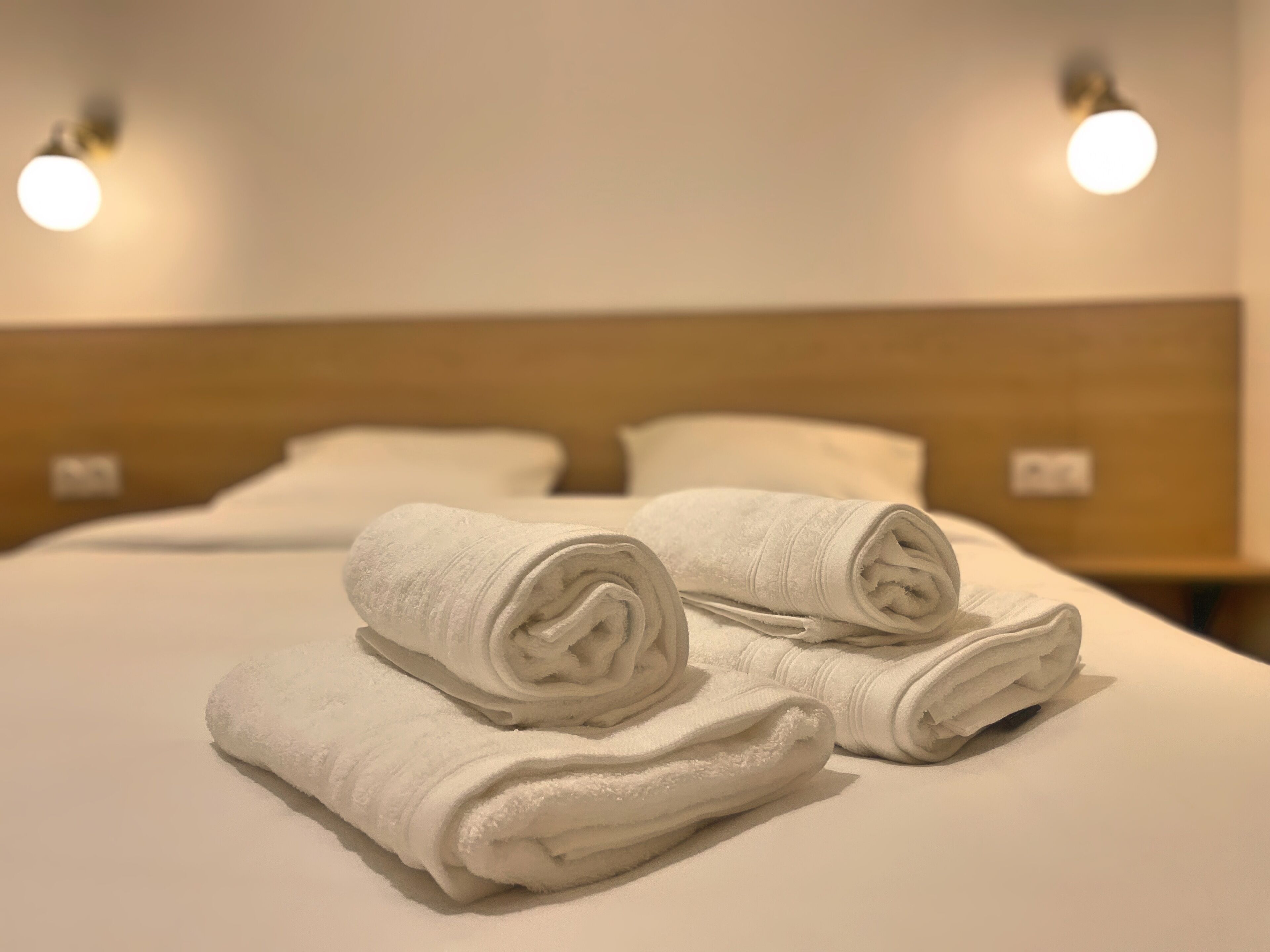 A neatly made bed with two rolled white towels and a wooden headboard.