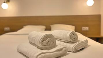 A neatly made bed with two rolled white towels and a wooden headboard.
