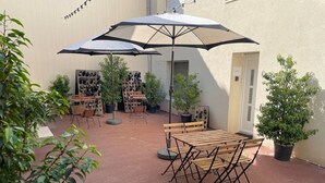 An outdoor patio area with wooden tables and benches, a large umbrella, and potted plants. - Les Fauvettes (Épernay)