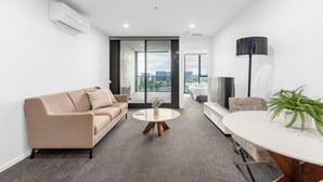 Un salon moderne avec un canapé, une table basse et un téléviseur. Il y a un balcon avec vue sur la ville.