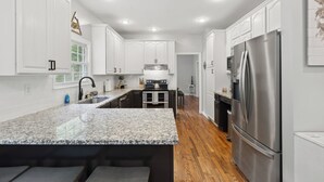 A modern kitchen with white cabinetry, a granite countertop, stainless steel appliances, and a wooden floor. - Hatton Hideaway at Red River Gorge! Pool / Hot Tub / Arcade Game Room (Stanton)