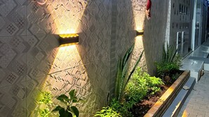 A building facade with patterned wall design, illuminated by warm lights, and bordered by a planter with green plants.