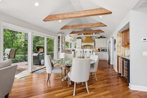 A spacious kitchen with wooden beams, a glass dining table, and a view of a deck.