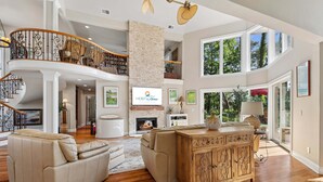Un salón espacioso con chimenea, una escalera de madera y ventanas grandes.