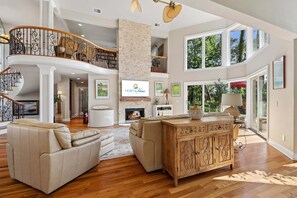 A spacious living area with a fireplace, a wooden staircase, and large windows.