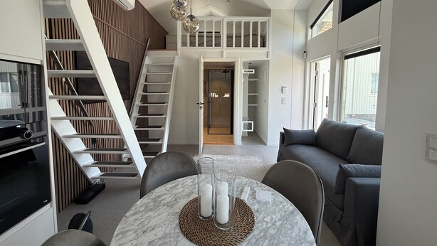 A modern interior with a dining area featuring a marble table, a staircase with a built-in shelf, and a grey sofa.