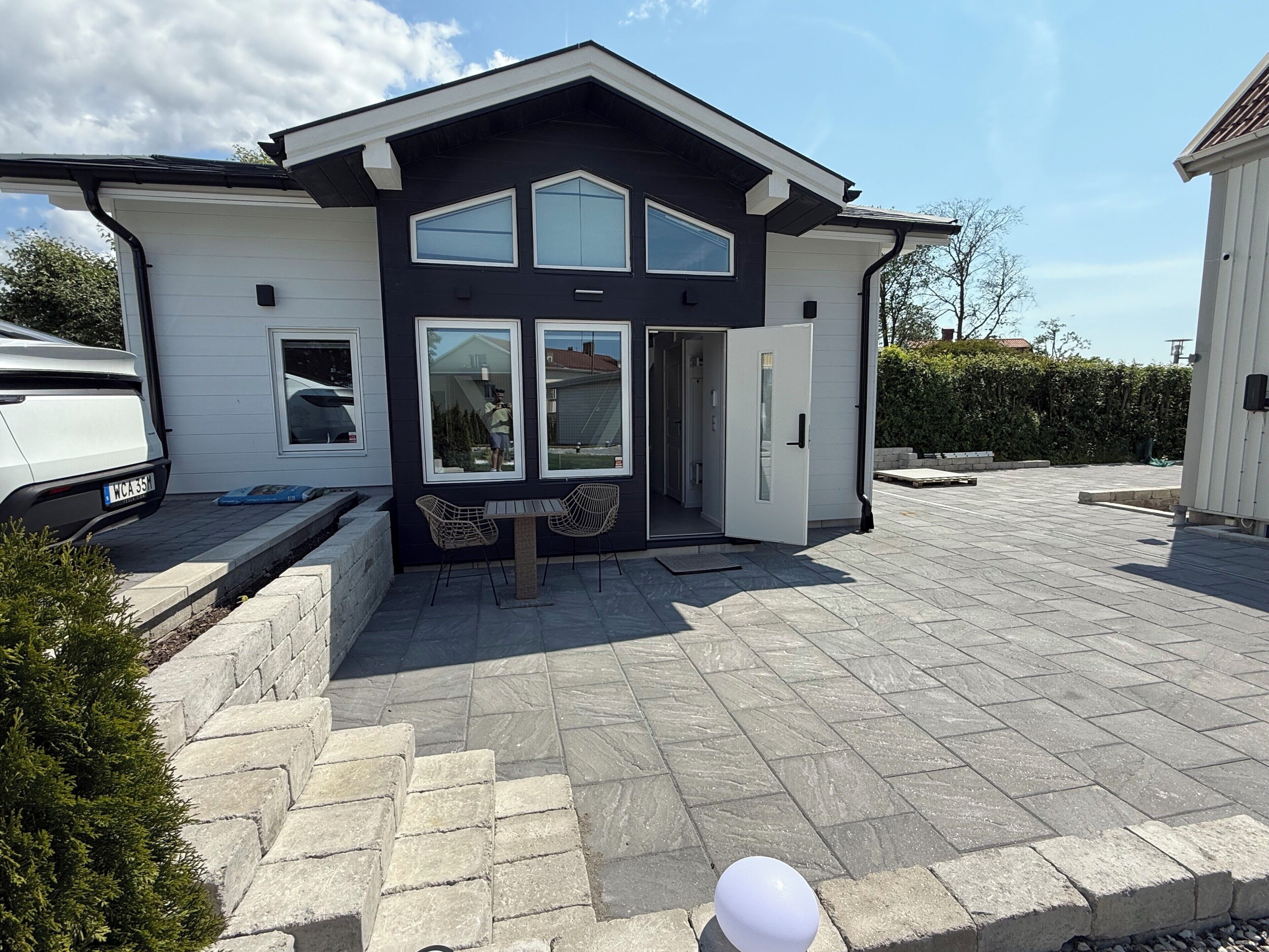 A modern two-story house with a patio area, a car parked in front, and a clear sky.