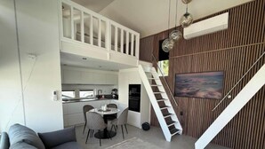 A modern living space with a grey sofa, a dining area with a round table, and a staircase leading to an upper level.