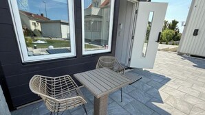 A patio with a table and two wicker chairs, a sliding glass door, and a view of a residential area.