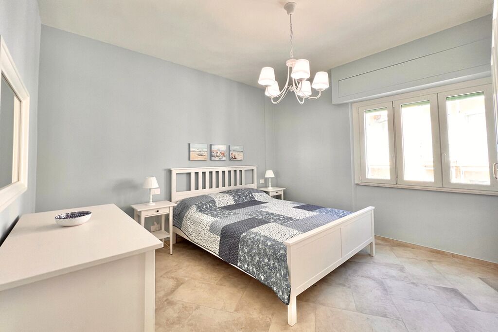 Une chambre à coucher avec un lit, des tables de chevet, une lampe, un lustre et une fenêtre.
