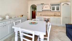 Une cuisine moderne avec des meubles blancs, une table à manger avec des chaises, et un canapé bleu en arrière-plan.
