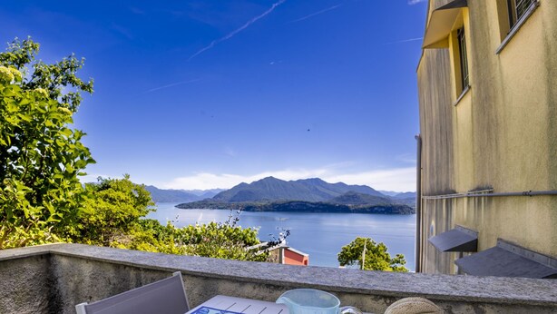 Una mesa con jarrón, plato y frutas, con vista a un lago y montañas al fondo.