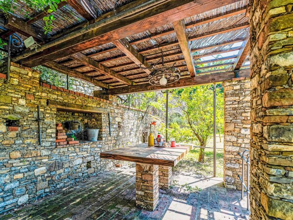 A rustic outdoor patio with a stone wall, wooden beams, and a table with various items.