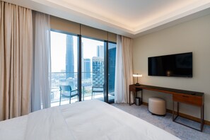 A hotel room with a large bed, a desk, a chair, a TV, and a view of the cityscape through large windows. - 2BR Address Dubai Opera | Walk to Mall, Burj Khalifa & Opera (Dubai)