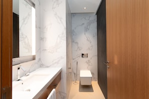 A modern bathroom with a marble backsplash, a white sink, and a toilet.