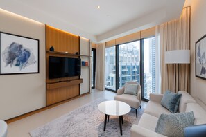 A modern living room with a flat-screen TV, a sofa, a coffee table, and a large window offering a city view. - 2BR Address Dubai Opera | Walk to Mall, Burj Khalifa & Opera (Dubai)