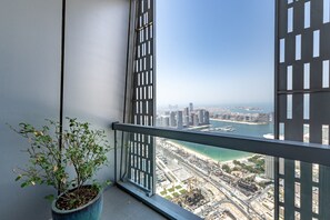 A balcony with a potted plant, a view of a coastal cityscape, and a clear sky.