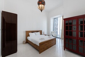 A bedroom with a wooden bed, a red cabinet, a window with blinds, and a hanging light fixture.