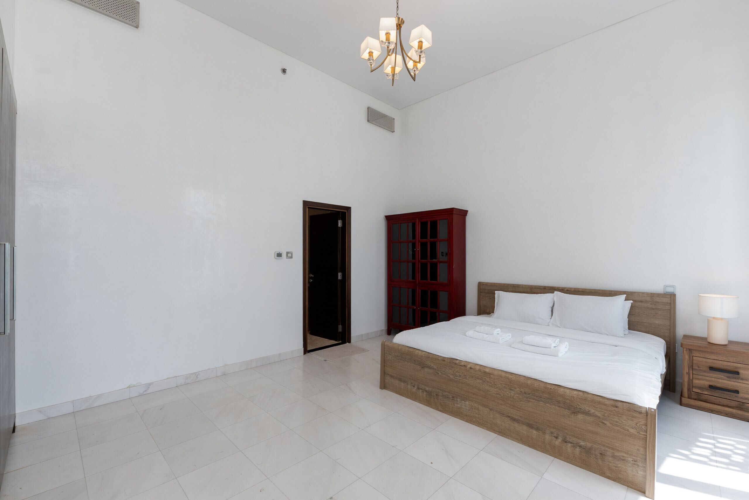 A spacious bedroom with a large bed, a wooden headboard, a nightstand, and a red cabinet.