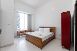 Ein modernes Schlafzimmer mit einem hölzernen Bett, weißen Bettwäsche, einem roten Kleiderschrank und Blick durch ein Fenster mit Jalousien.