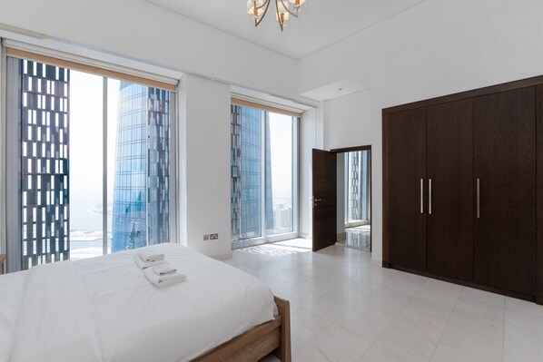 A modern hotel room with a large bed, a wardrobe, and floor-to-ceiling windows offering a city view.