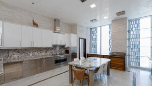 Une cuisine moderne avec des meubles blancs, un plan de travail en marbre, une table à manger avec des chaises et une grande fenêtre offrant une belle vue.
