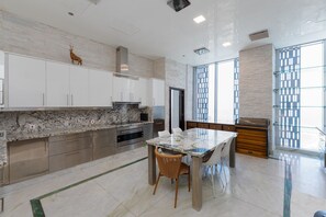 A modern kitchen with white cabinets, a marble countertop, a dining table with chairs, and a large window with a view.