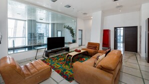 Un salon moderne avec des canapés en cuir, un téléviseur à écran plat et une grande fenêtre donnant sur la ville.