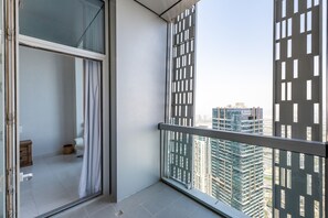 Ein Balkon mit Blick auf hohe Gebäude, eine Glastür und ein kleiner Holzschemel.