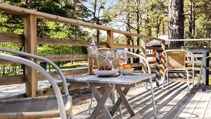 Terraza de madera con mobiliario exterior, incluyendo una mesa con una botella, vasos y un cuenco de fruta.