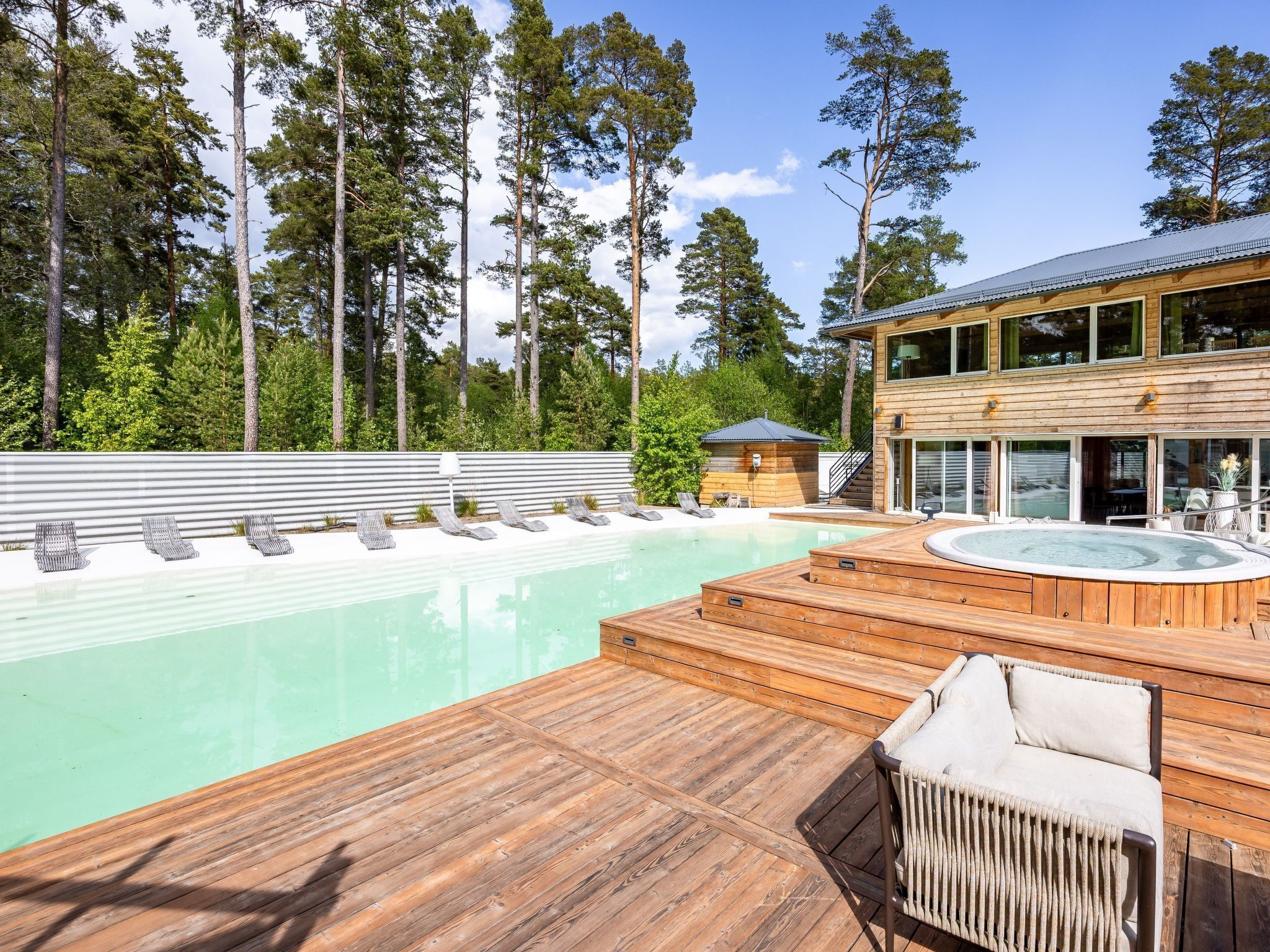 A wooden deck with a hot tub, lounge chairs, and a pool.