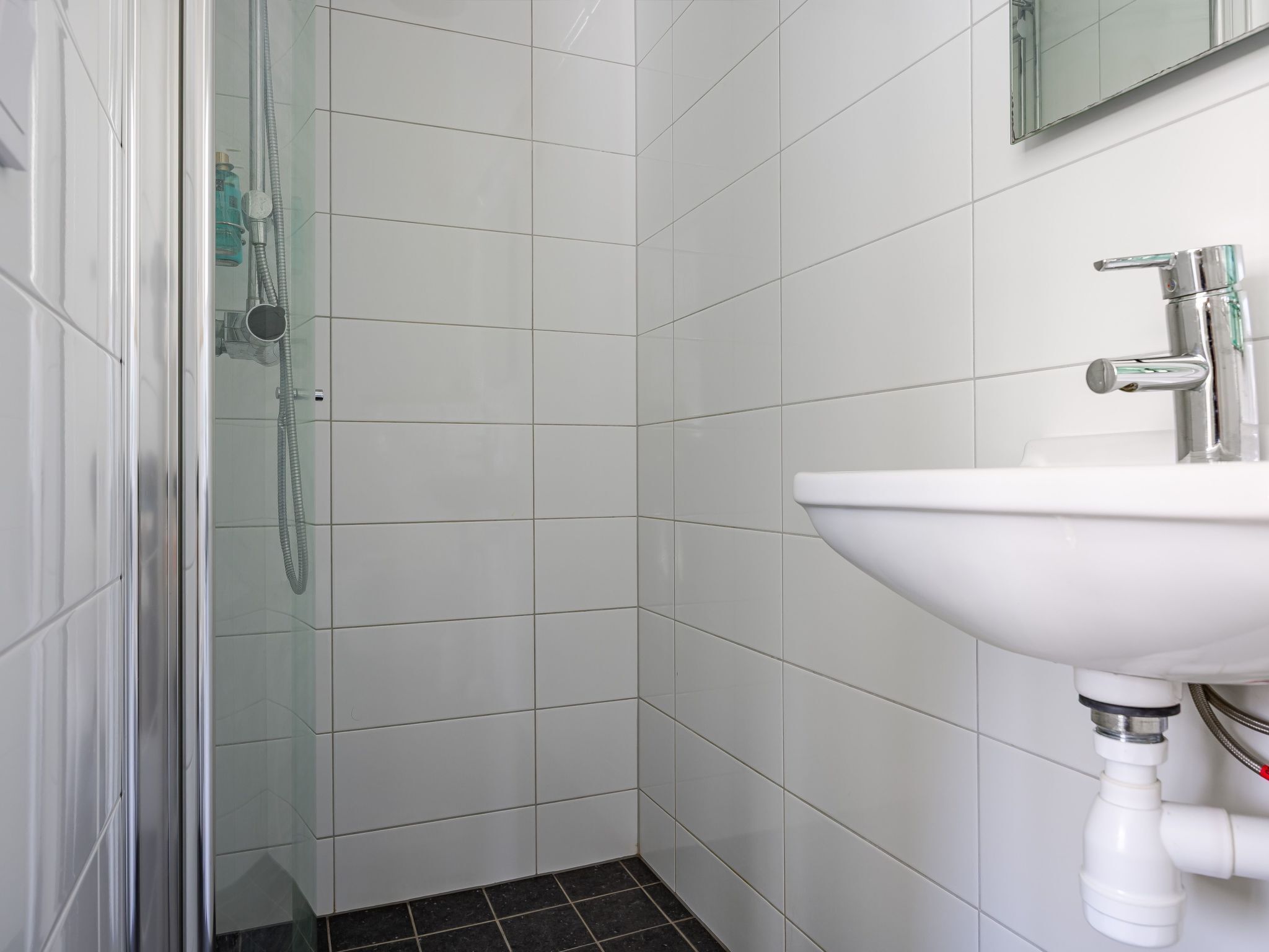 A bathroom with white tiles, a glass shower enclosure, and a white sink with a chrome faucet.