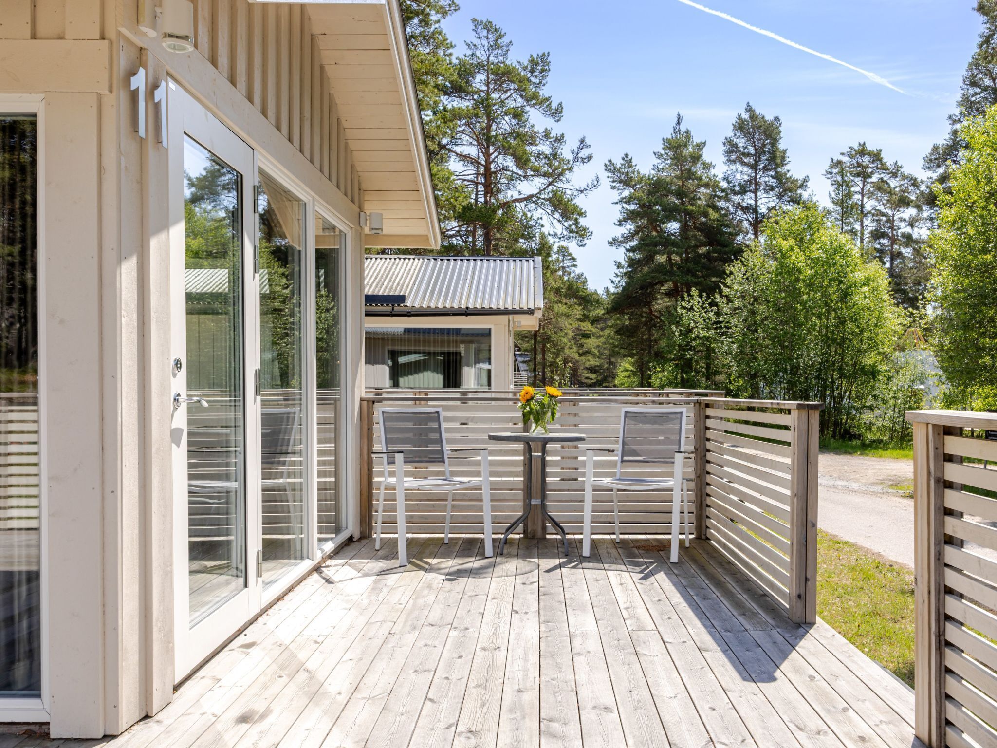 Een houten terras met buitenmeubels, een tafel met een bloevas en uitzicht op het omliggende bos.
