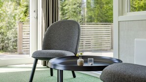 A modern room with a grey upholstered chair, a small round table, and a view of a green outdoor area through large windows. - Hölick Minichalet Plus 6 by Interhome (Hölick)