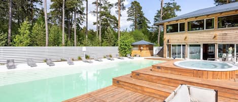 A wooden deck with a hot tub, lounge chairs, and a pool.