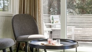 Una habitación moderna con una butaca gris tapizada, una mesa redonda negra con velas, y vistas a un balcón con mobiliario exterior.