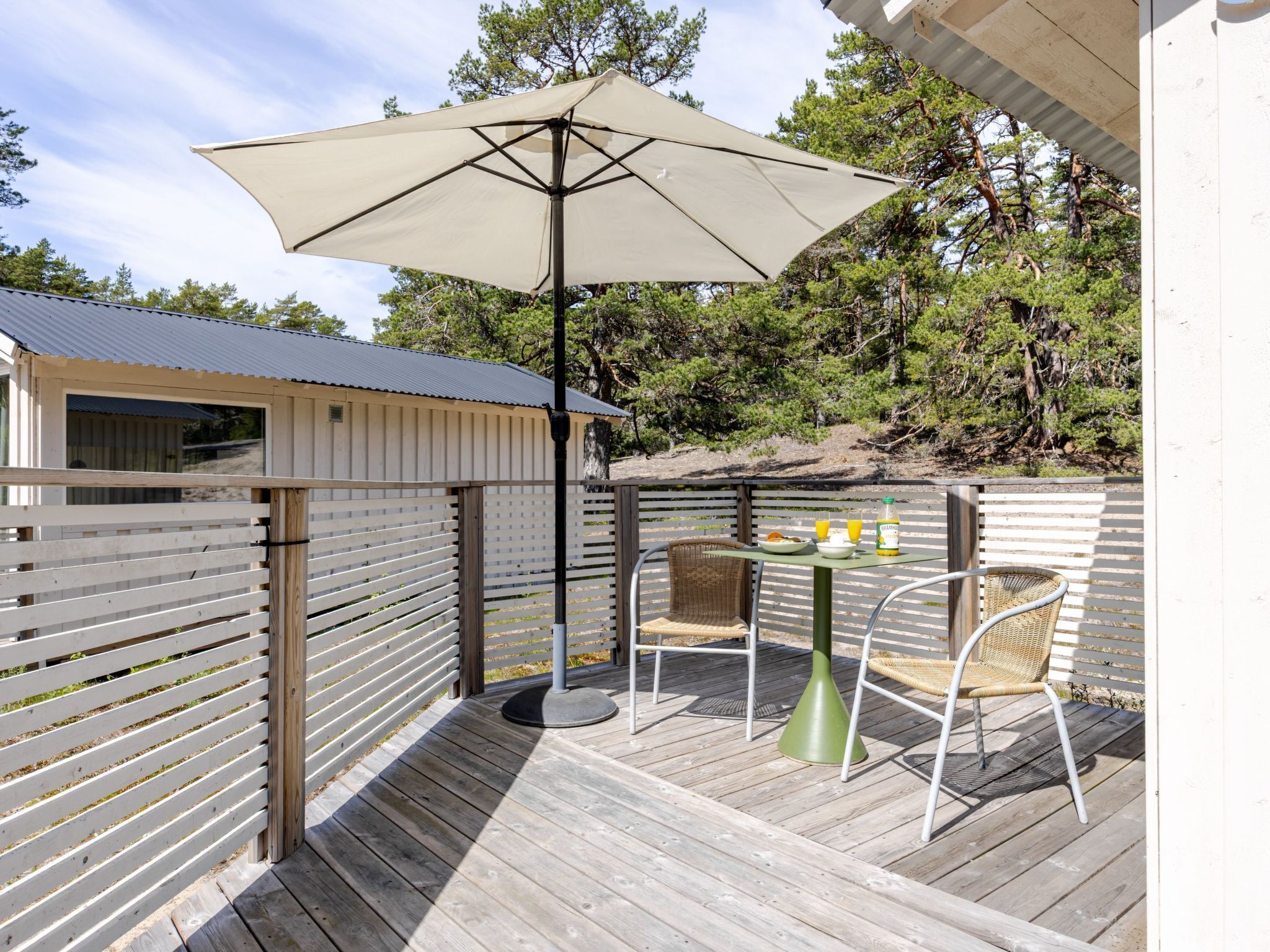 Een houten terras met een tafel, stoelen en een parasol, en een klein gebouw met een raam.