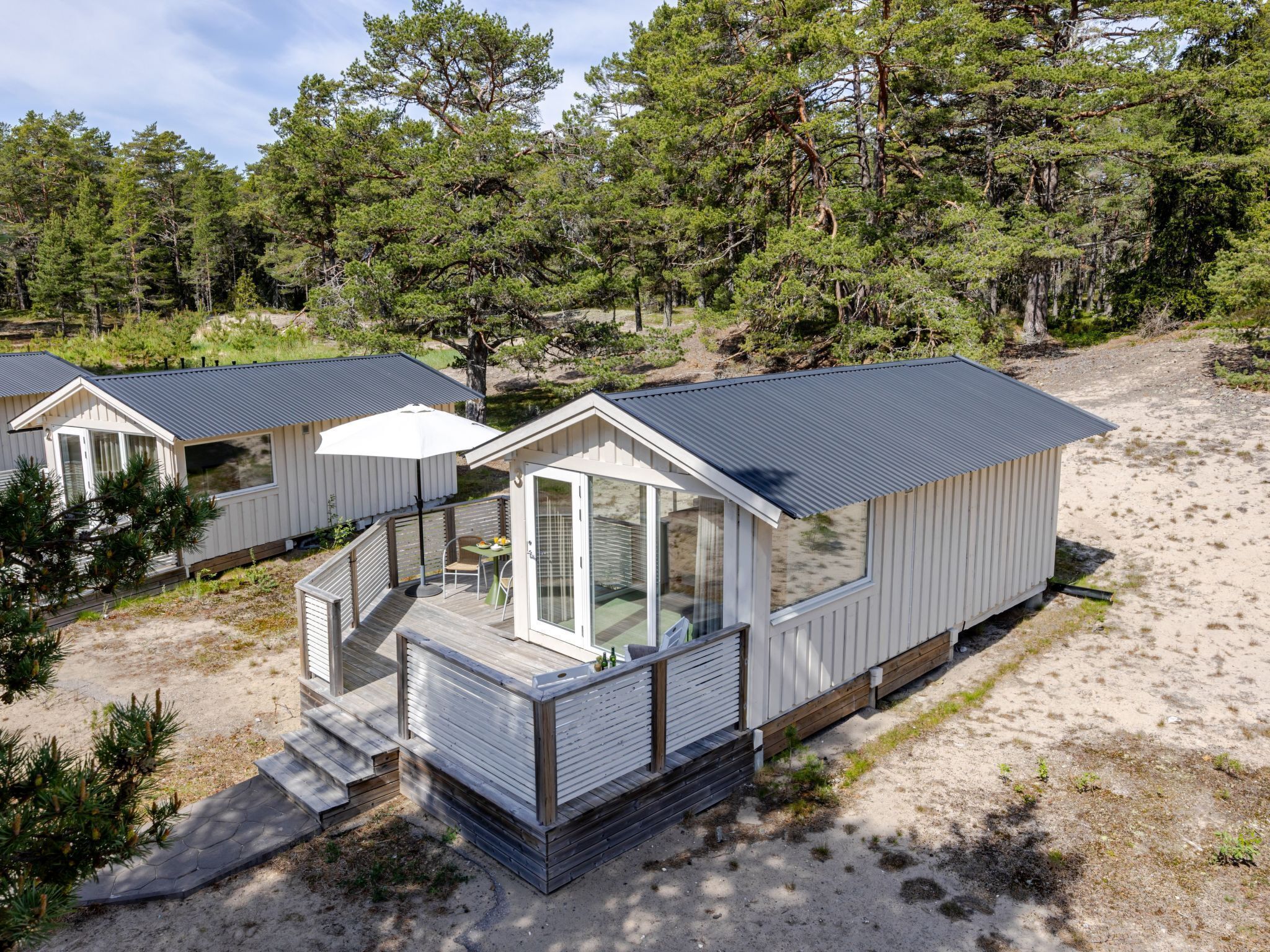 Une petite cabane à un seul étage, dotée d’un balcon et entourée d’arbres et de sable.