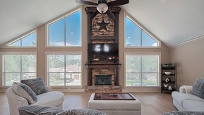 A spacious living room with a stone fireplace, large windows, and a high ceiling fan. - "Fitz-Just-Right" home in Walden: Boat ramp, Pickleball, Community Pools! (Montgomery)