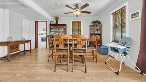 A dining area with wooden chairs and a high table, a ceiling fan, and a baby high chair.