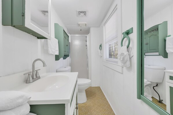 Une salle de bain avec un lavabo blanc, des meubles verts, des toilettes blanches et un miroir avec un cadre vert.
