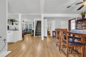 Un vaste espace de vie doté d’un plancher en bois, d’une table à manger avec des chaises, d’un escalier et d’un coin cuisine avec des armoires blanches et un comptoir.