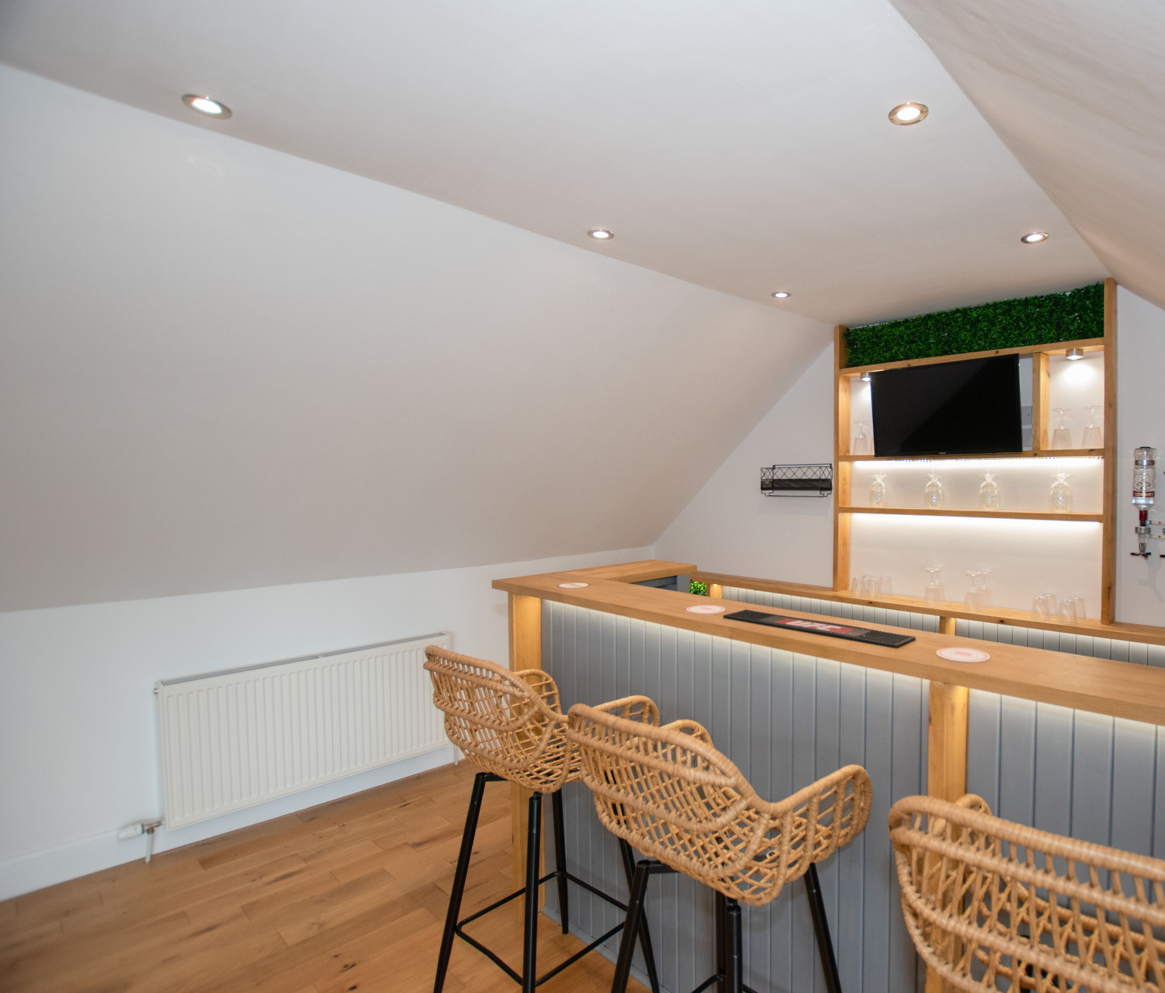 A modern bar area with a wooden counter, three wicker chairs, and a green wall decoration.