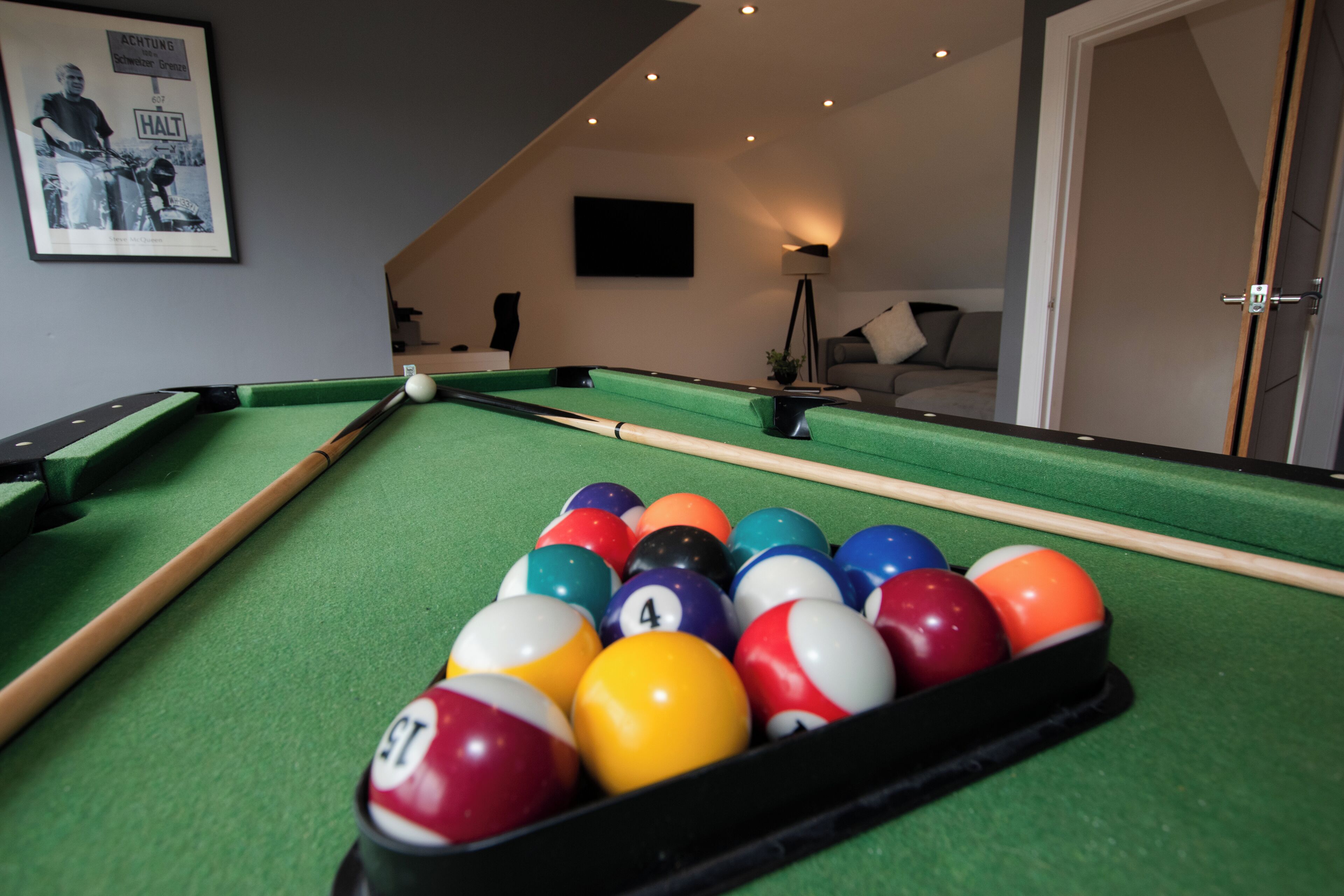 A pool table with balls, a framed picture on the wall, a lamp, and a sofa in the background.