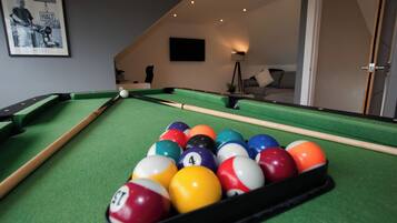 A pool table with balls, a framed picture on the wall, a lamp, and a sofa in the background.