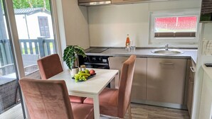 A modern kitchen with a dining area, featuring a table with chairs, a window with a view of the outdoors, and a countertop with a sink and a stove. - Vacation home Joschi by Interhome (Plau am See)