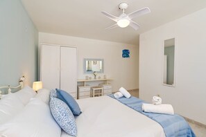 A hotel room with a bed, a desk, a chair, a vanity with a mirror, and a ceiling fan.