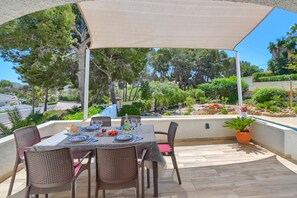 An outdoor patio with a table set for dining, surrounded by wicker chairs, under a canopy.