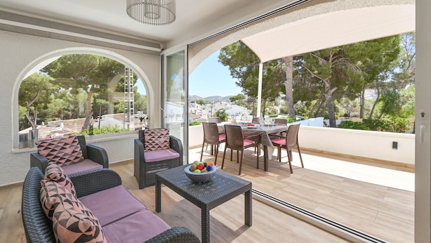 Un patio iluminado por el sol con mobiliario de mimbre, una zona de comedor y vistas del paisaje circundante.